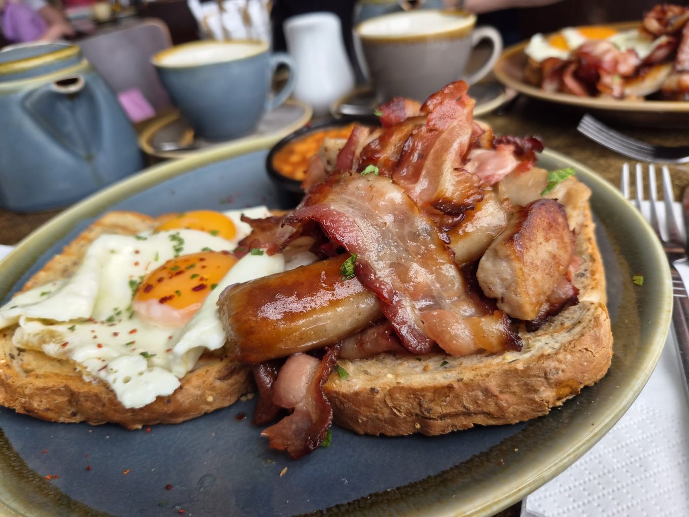 A cooked breakfast: bacon, sausages and fried eggs on toast
