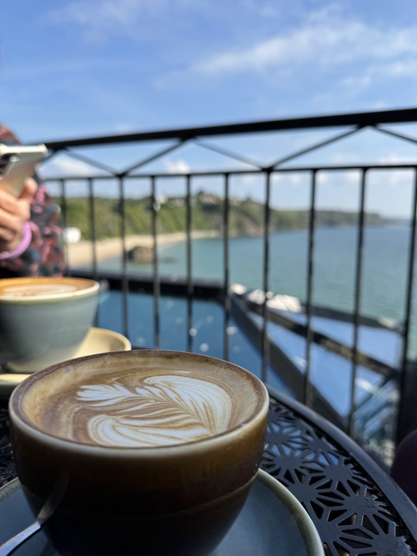 A cappuccino on a terrace table, with Tenby bay and beach below