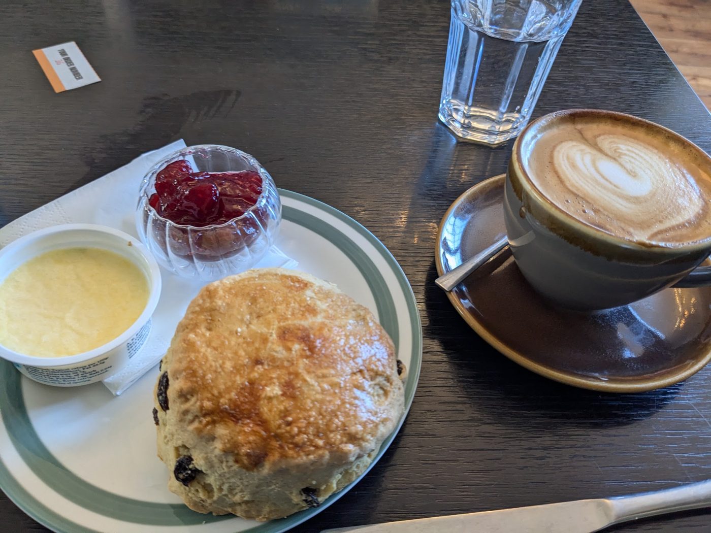A scone with cream and jam, and a cappuccino